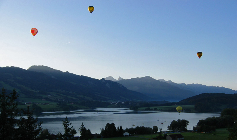 Terwijl de zon zijn eerste stralen van achter de bergtoppen over het meer laat schijnen, stijgen een aantal ballonnen op