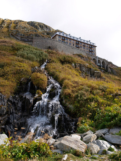 Een mini waterval langs de weg met rechtsboven hotel/restaurant 'Gletscher Belvedere'.